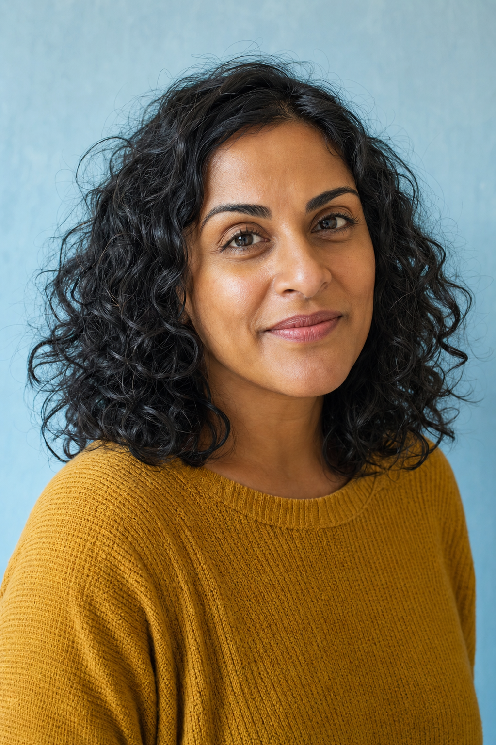 Maya Calder, PetPetCat pet care editor, in a mustard knit top against a pale blue background